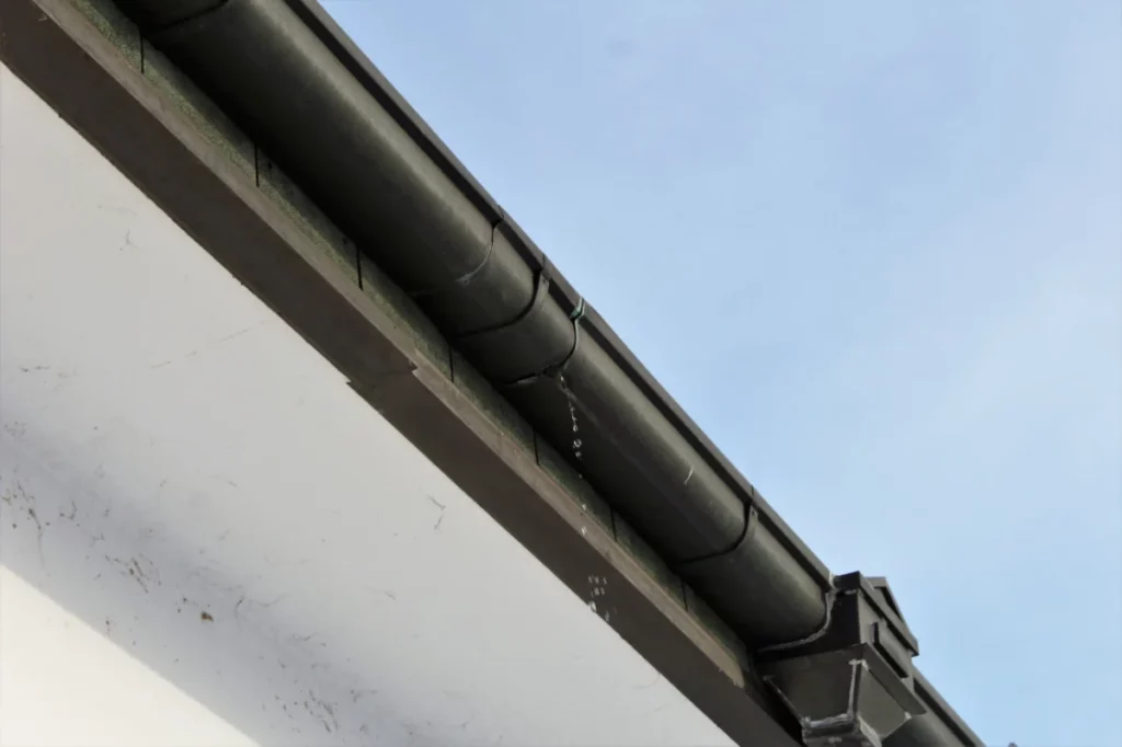 Signs your gutters need repair: A leaking gutter with water dripping down, highlighting damage caused by wear and poor maintenance